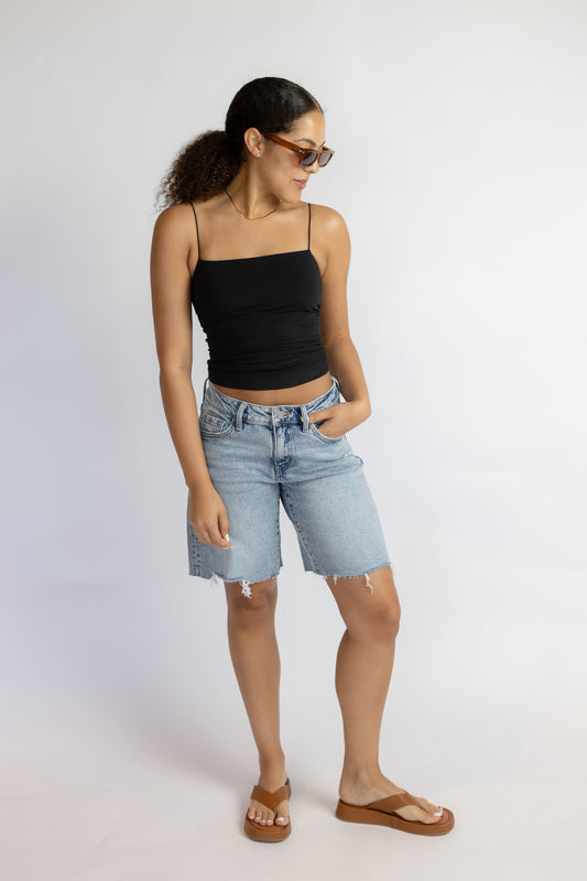 Woman wearing a black tank top and light blue denim shorts on a white background