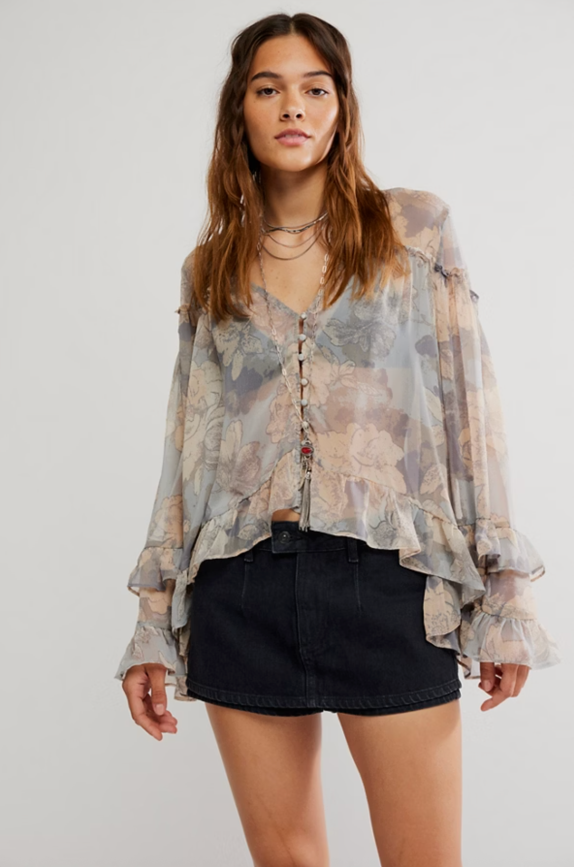Woman wearing sheer long sleeve blouse with muted floral print, ruffle hem and sleeves, styled with black mini skirt