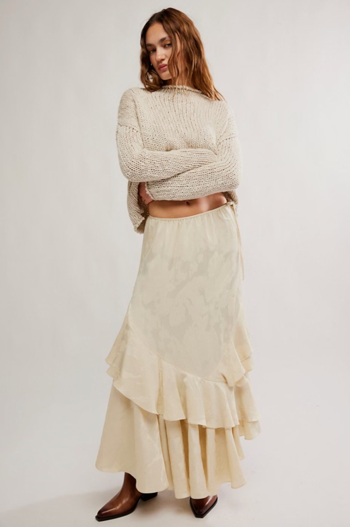 Woman wearing champagne jacquard floral maxi skirt with asymmetrical ruffle hem and side tie detail, paired with chunky knit sweater and brown boots