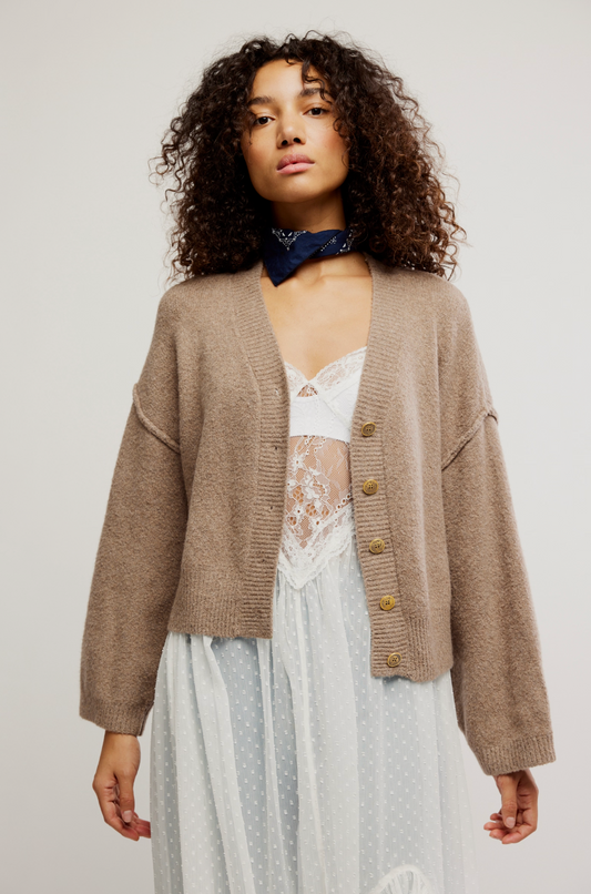 Woman wearing a brown cardigan over a white dress with a blue scarf on a plain background