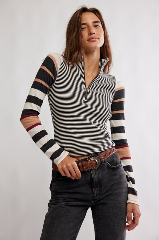 Woman wearing a striped half-zip long sleeve knit top with mixed stripe sleeves and ribbed texture tucked into dark denim jeans.