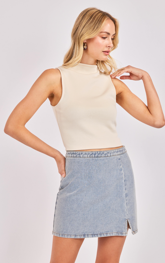 Woman wearing a cream high-neck sleeveless crop top paired with a light wash denim mini skirt.