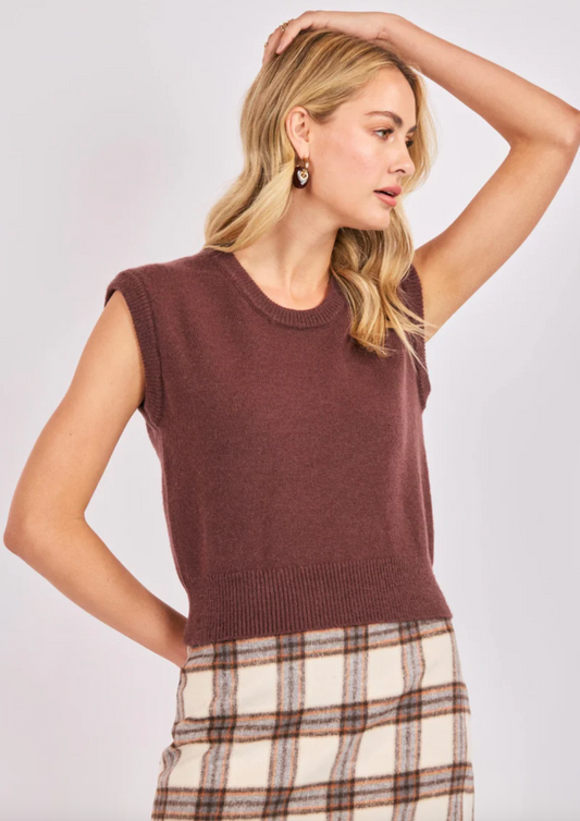 Woman wearing a brown knit sweater vest paired with a plaid skirt.
