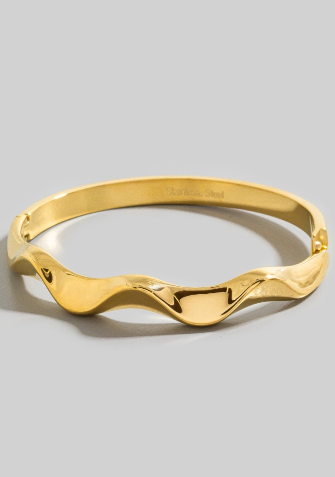 Gold bracelet with wavy design on a gray background