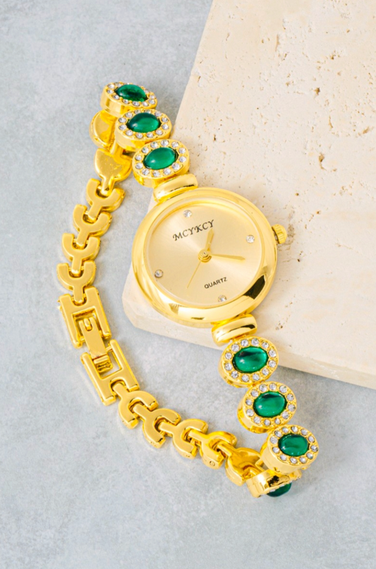 Gold watch with green gemstones on a light gray background
