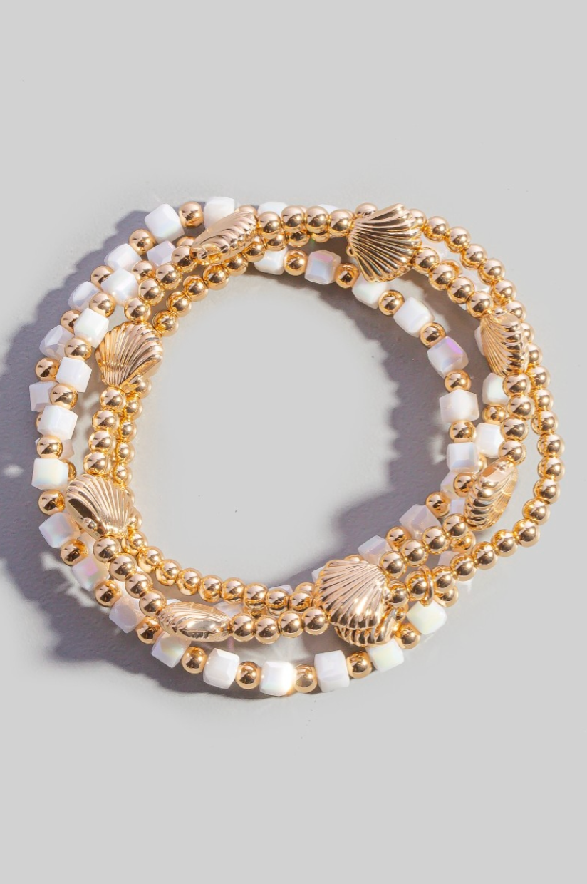 Set of gold and white beaded bracelets on a light gray background