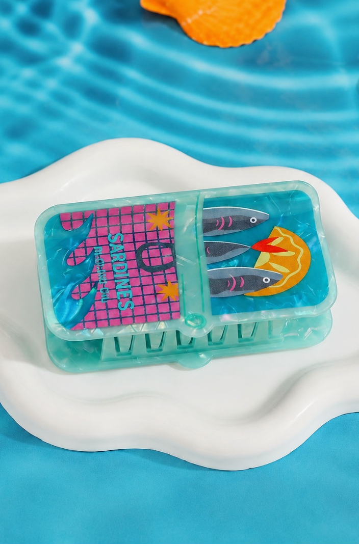 Teal vintage sardine tin inspired hair claw clip with colorful fish illustration and glossy marbled acetate finish.
