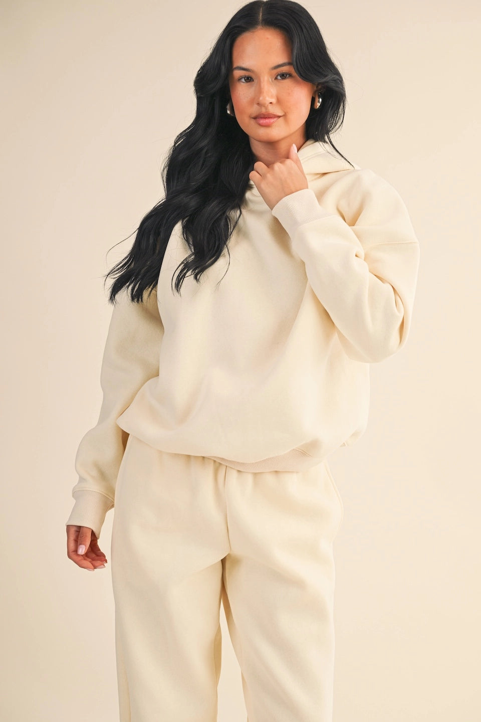 Woman wearing oversized cream fleece hoodie with relaxed fit and soft drape.