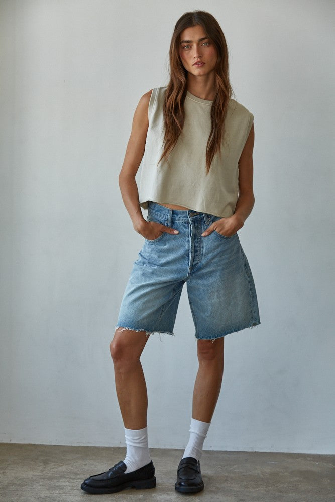 Woman wearing pigment-dyed beige sleeveless cotton tank with light wash denim bermuda shorts and black loafers