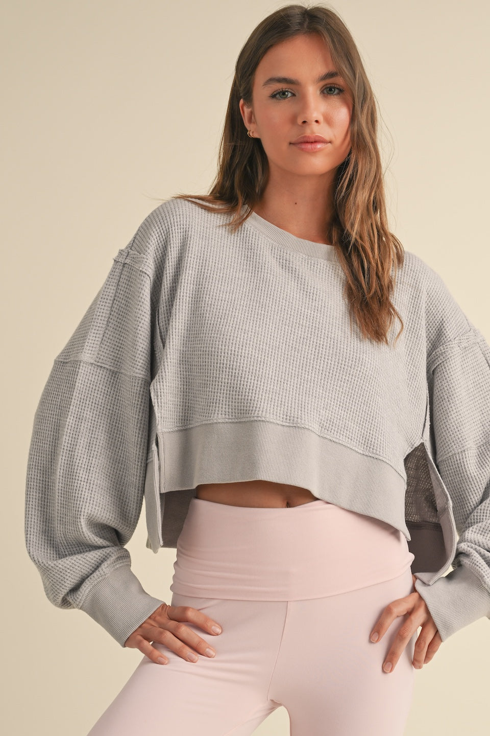 Woman wearing light gray cropped waffle knit pullover sweater with oversized sleeves and relaxed fit.