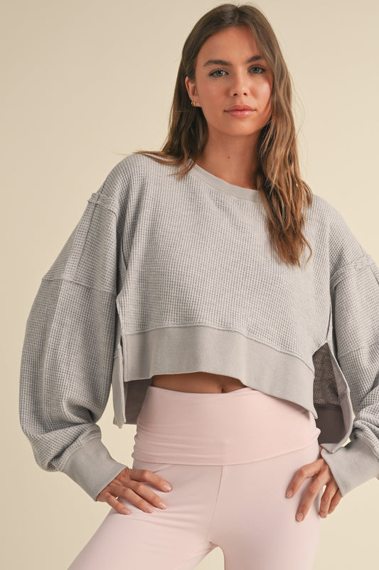Woman wearing light gray cropped waffle knit pullover sweater with oversized sleeves and relaxed fit.