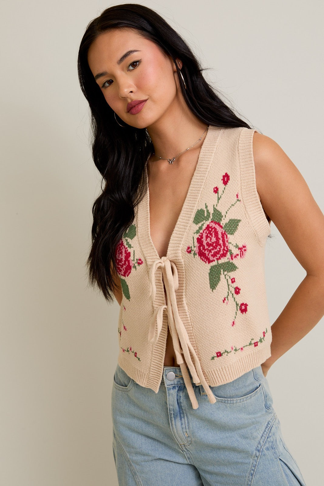Model wearing Rose Bloom Knit Vest, a beige knit vest with red rose graphics and tie-front closure.
