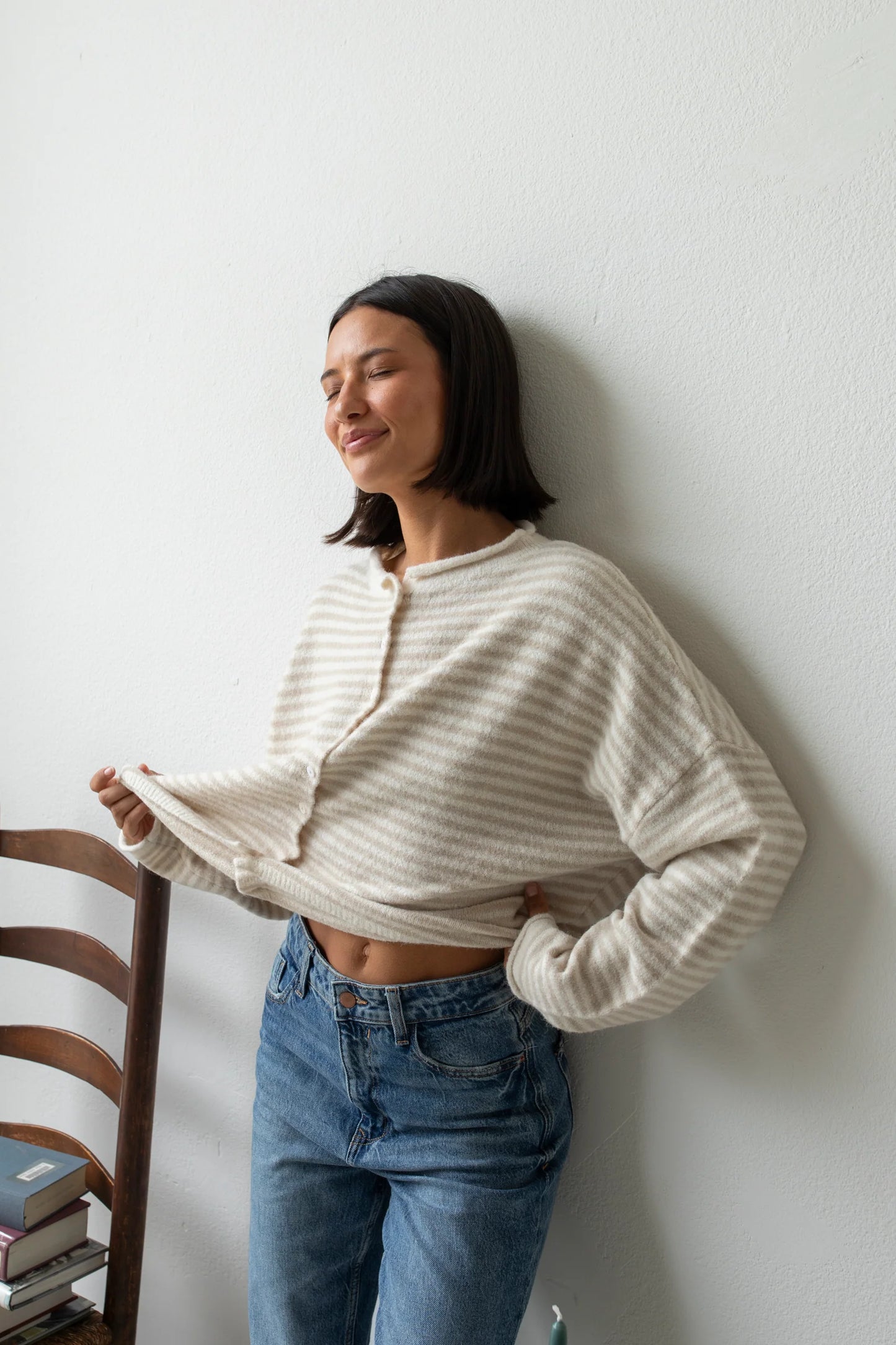 Woman wearing a cream and beige striped lightweight cardigan with rolled edges and button-front closure styled with high-waisted jeans.