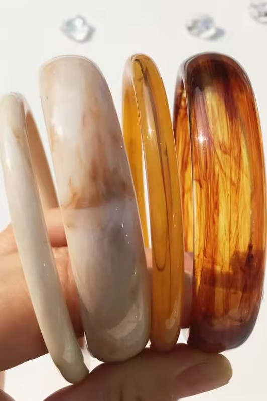 Three amber-colored bangles held in a hand against a white background