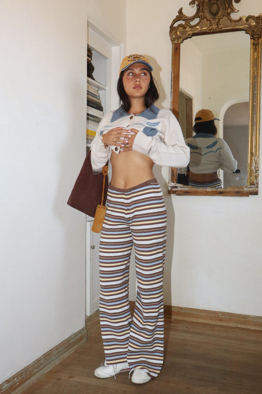 Person wearing a white sweater with blue accents and striped pants, standing in front of a mirror.