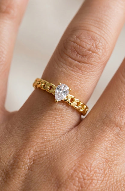 Adjustable gold curb chain ring featuring a pear-cut cubic zirconia center stone with a polished gold finish and open-back design.
