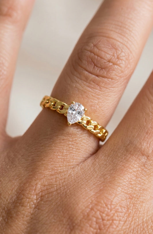Adjustable gold curb chain ring featuring a pear-cut cubic zirconia center stone with a polished gold finish and open-back design.

