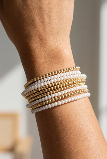 Layered stretch bracelet set featuring pearl-tone and gold-tone beaded strands for an elegant stacked bracelet look.