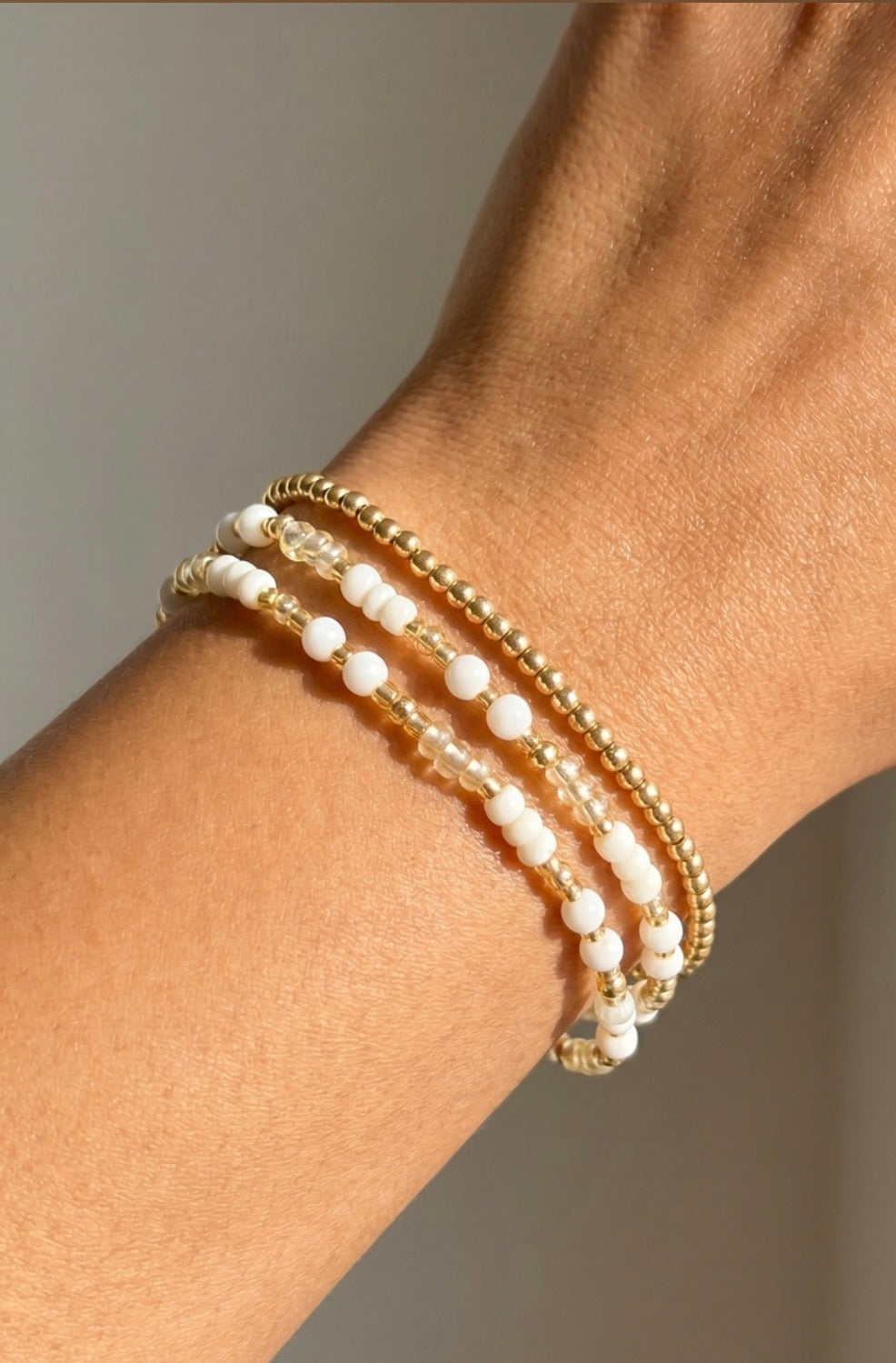 Three-piece stretch bracelet set featuring gold ball beads, iridescent shell beads, and ivory seed beads in a layered coastal-inspired design.
