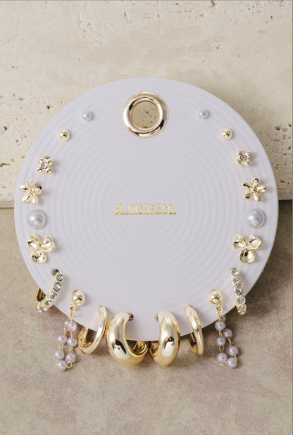 Gold-tone multi-pair earring set featuring floral studs, pearl studs, crystal hoops, chunky huggies, and classic gold earrings for mix-and-match styling.