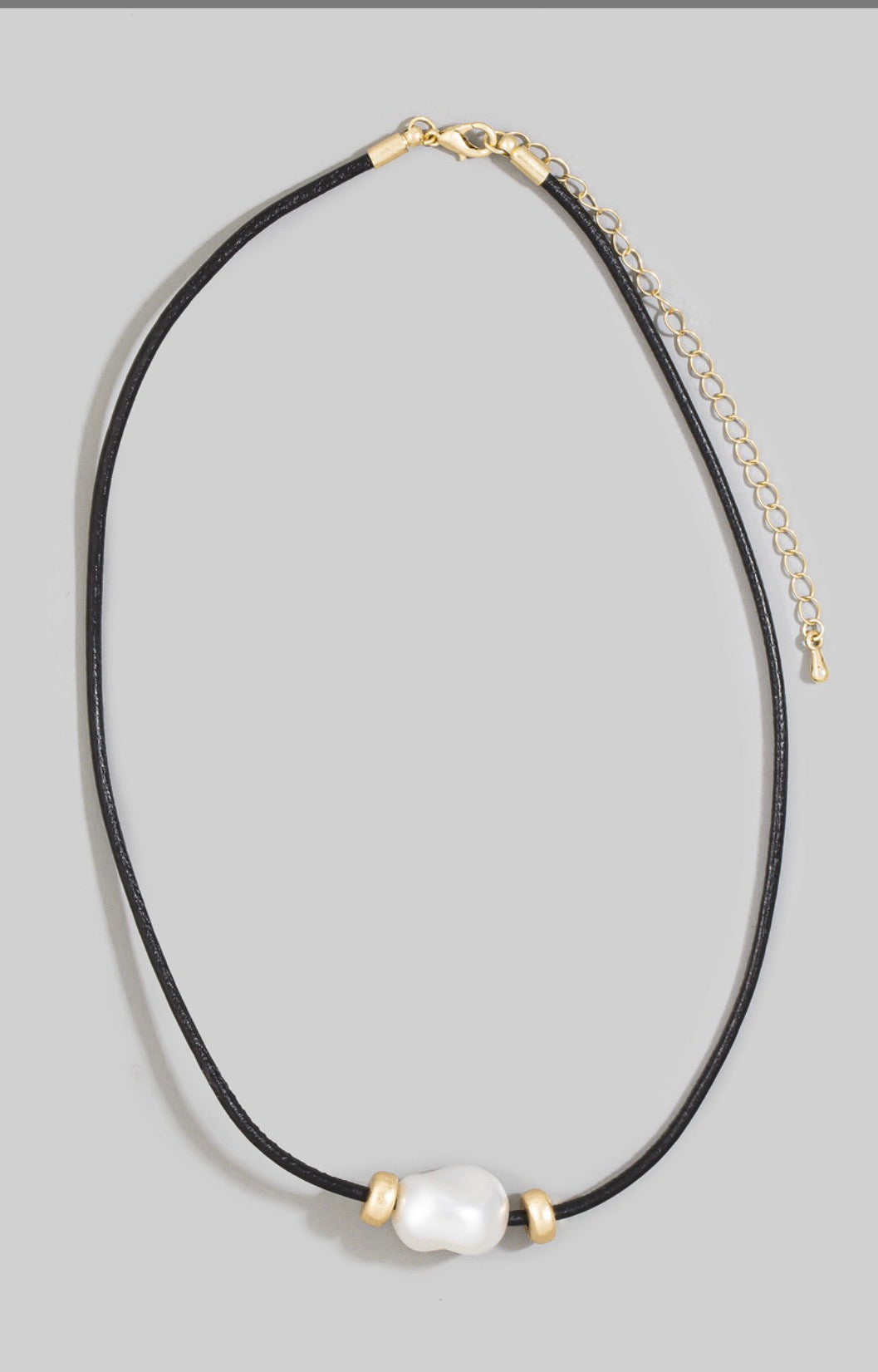 Black leather cord necklace featuring an oversized baroque-style ceramic pearl with gold-tone spacer accents and an adjustable chain closure.
