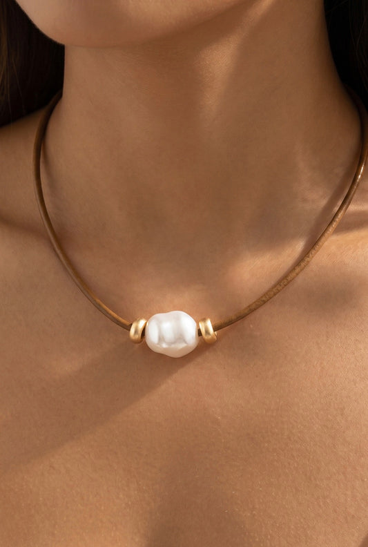 Brown leather cord necklace featuring an oversized baroque-style ceramic pearl with gold-tone spacer accents and an adjustable chain closure.