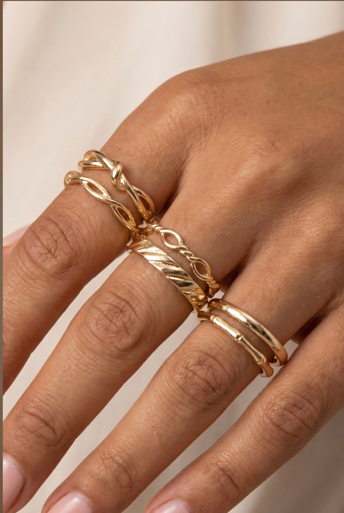 Five-piece gold textured ring stack featuring twisted, woven, Figaro chain, dome, and engraved bands for a layered everyday look.