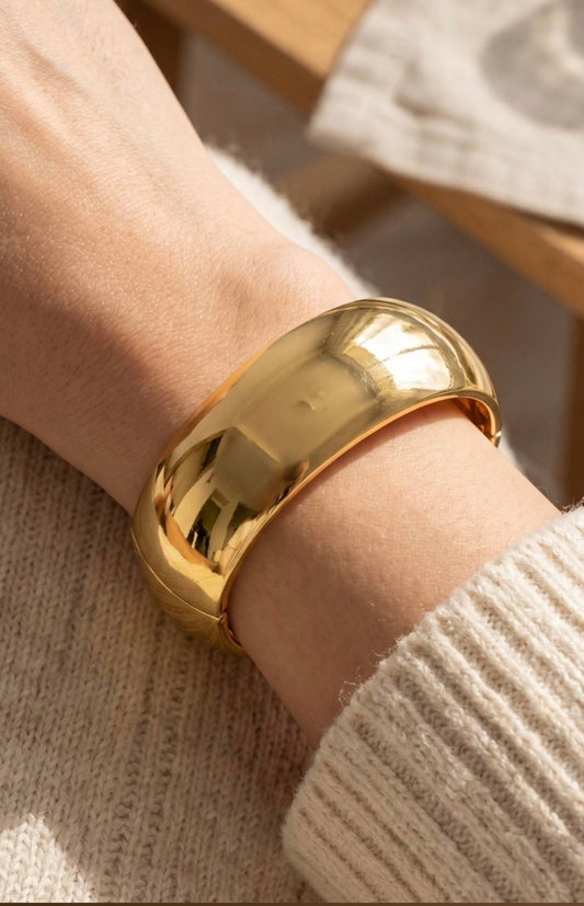 Wide gold dome bangle bracelet with a smooth polished finish and hinged closure for a bold, modern statement look.