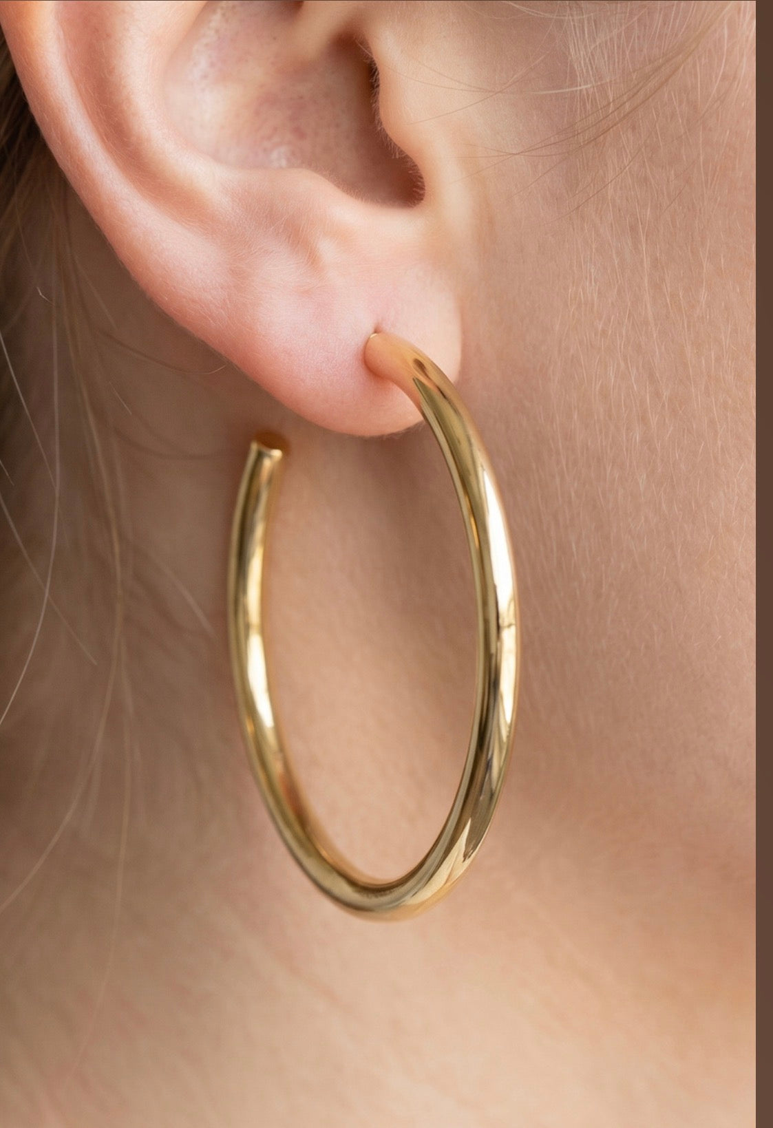 Large polished stainless steel open hoop earrings with a smooth tubular design worn on the ear.