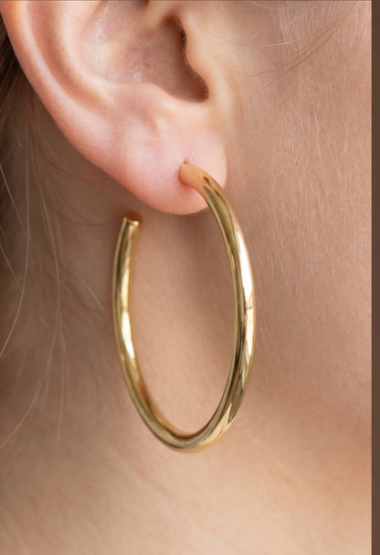 Large polished stainless steel open hoop earrings with a smooth tubular design worn on the ear.