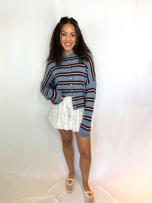 Woman wearing a striped sweater and white skirt against a plain background