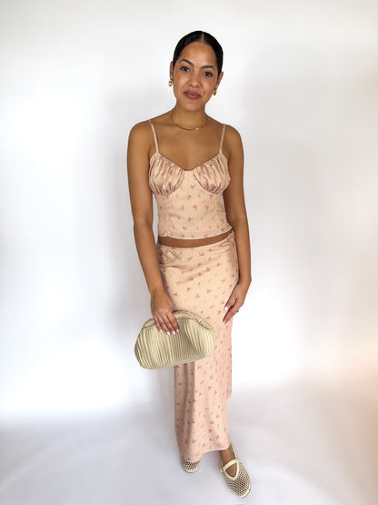 Woman wearing a beige patterned outfit holding a clutch against a white background