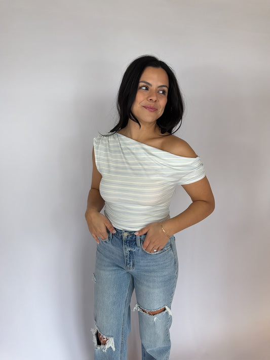 Model wearing a striped one shoulder knit top styled with light wash distressed denim