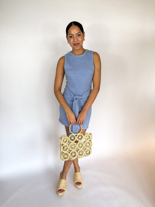 Woman in a blue dress holding a woven handbag against a white background