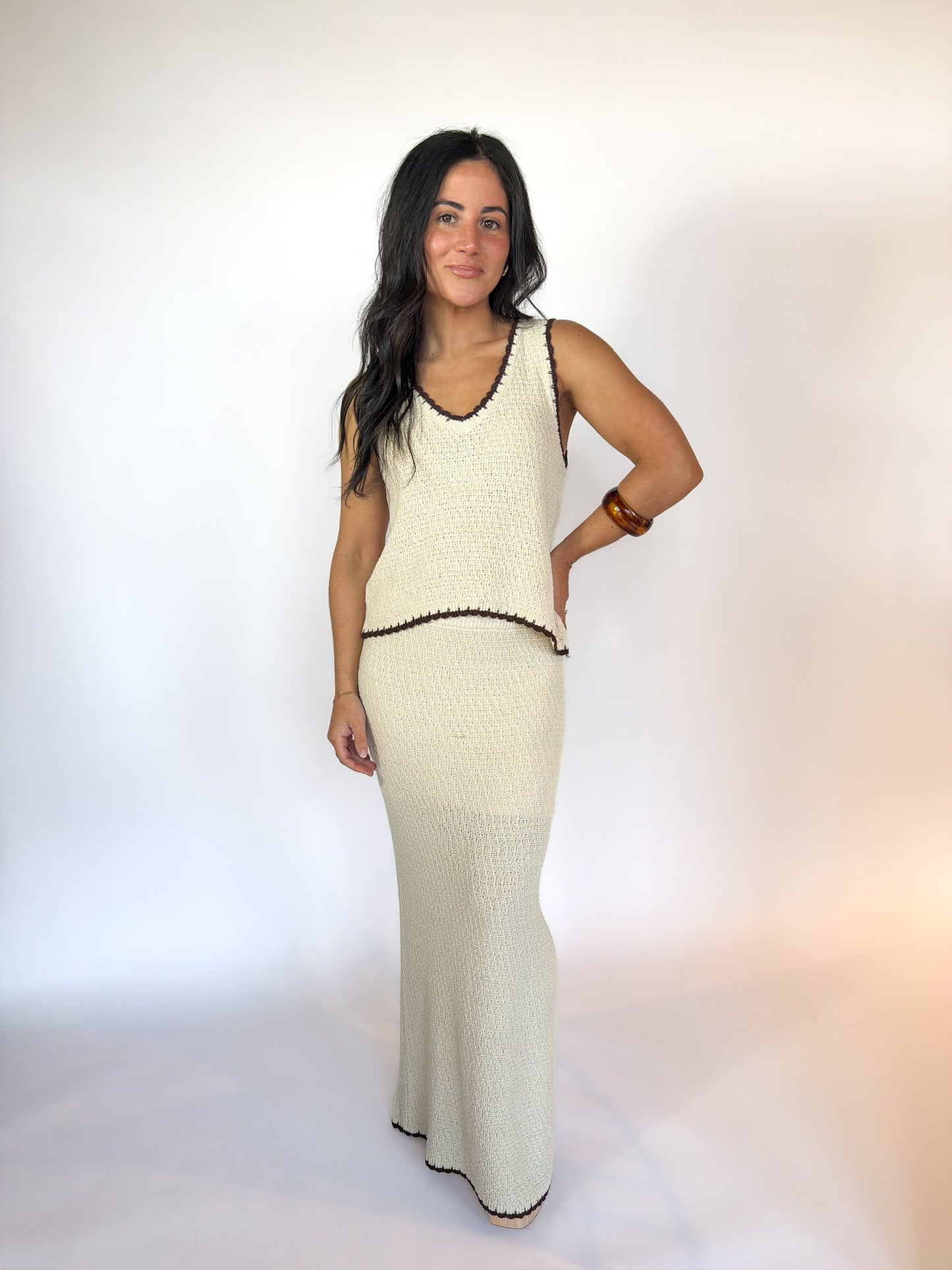 Woman wearing a long cream-colored dress with black trim against a white background