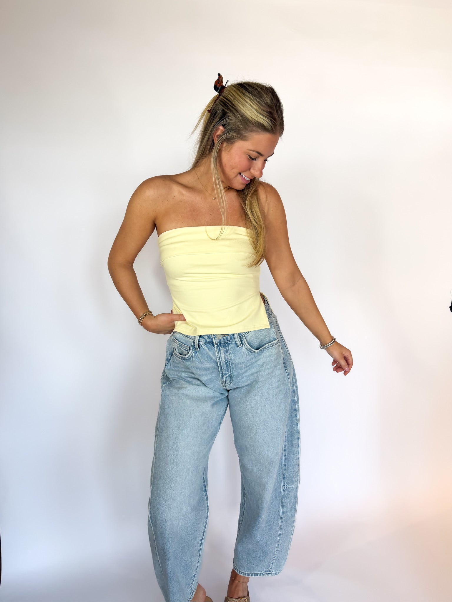 Woman wearing a yellow strapless top and light blue jeans against a white background