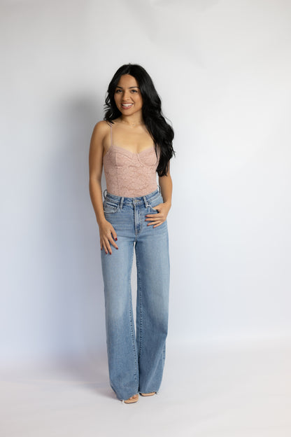 A woman modeling a light pink lace camisole top and high-waisted, wide-leg light blue jeans against a plain white studio background.