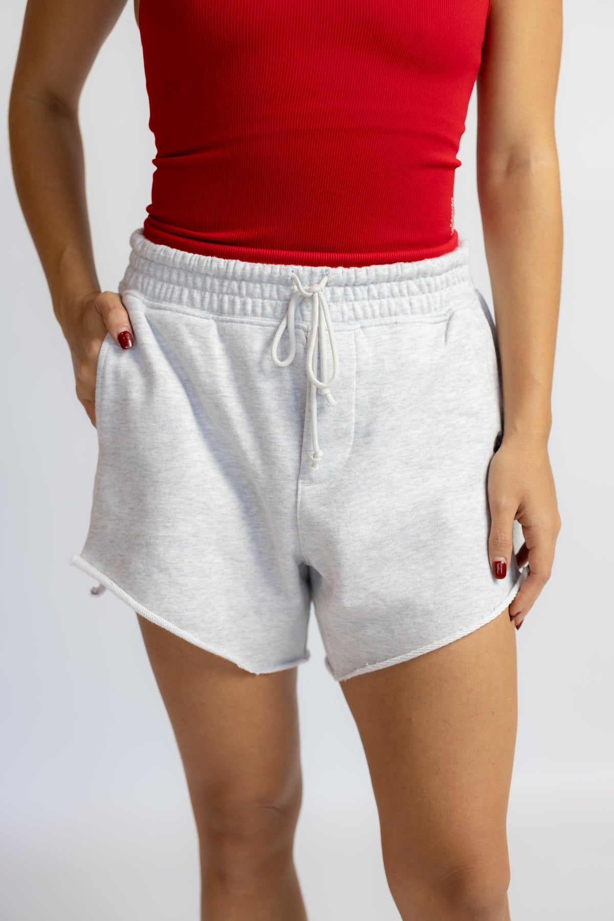 A person wearing light heather gray drawstring shorts and a red ribbed top, shown from the chest to the upper thighs against a plain light gray studio background.