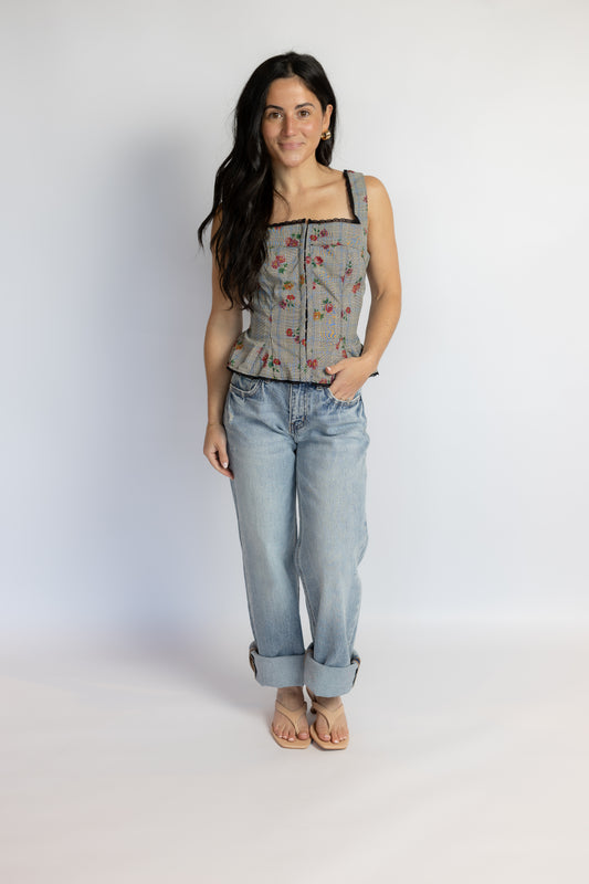 A woman modeling a sleeveless gray floral corset-style top paired with light-wash blue jeans and tan sandals, standing against a plain light gray studio background.