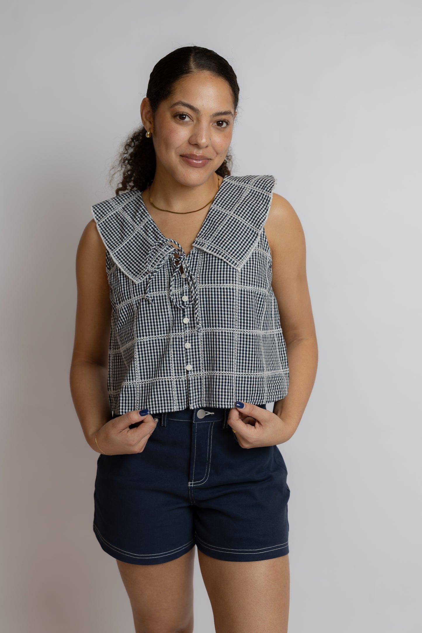 Woman wearing a sleeveless checkered top and dark shorts against a plain background