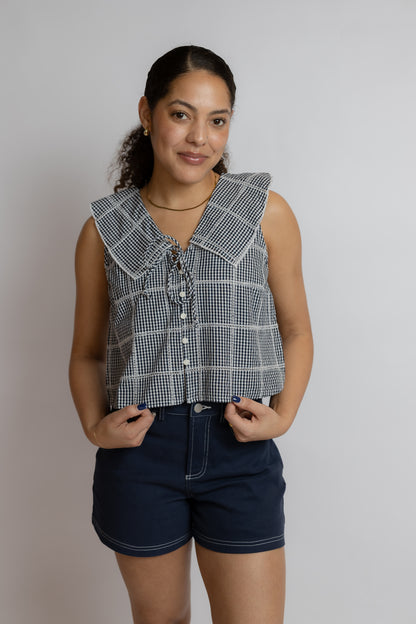 Woman wearing a sleeveless checkered top and dark shorts against a plain background