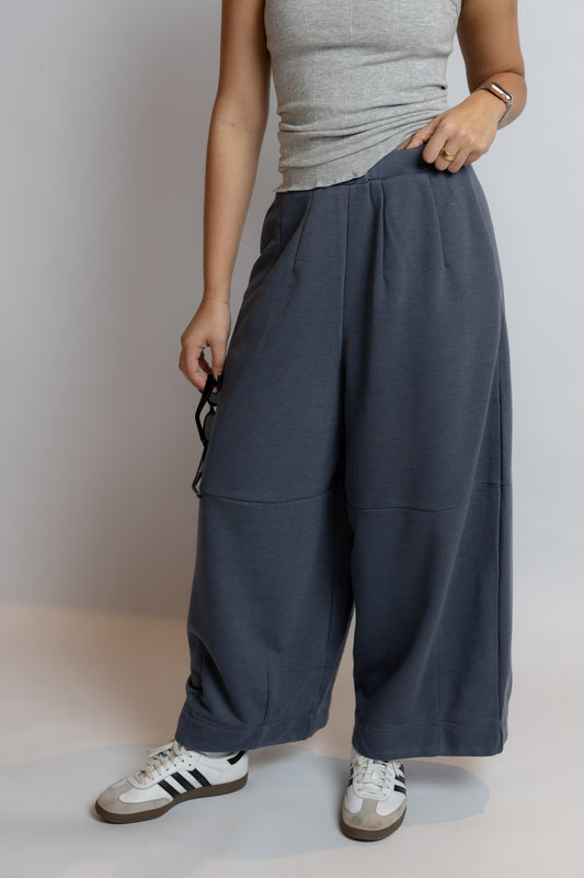 Person wearing gray tank top and wide-leg pants with white sneakers on a plain background