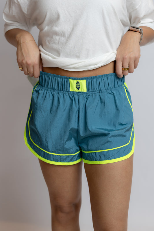 Person wearing blue shorts with green accents on a plain background