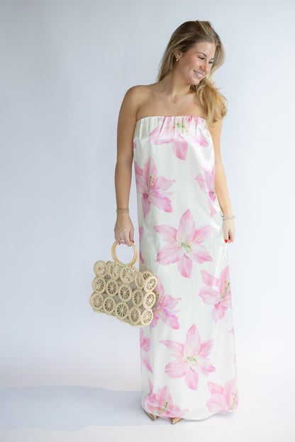 Woman wearing a strapless floral dress holding a gold clutch against a white background