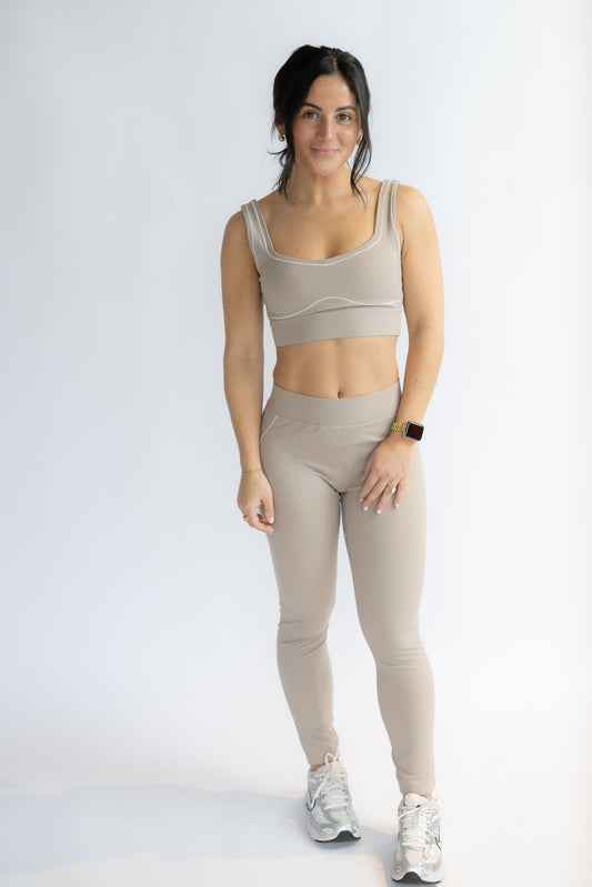 Woman wearing a beige sports bra and leggings set on a white background