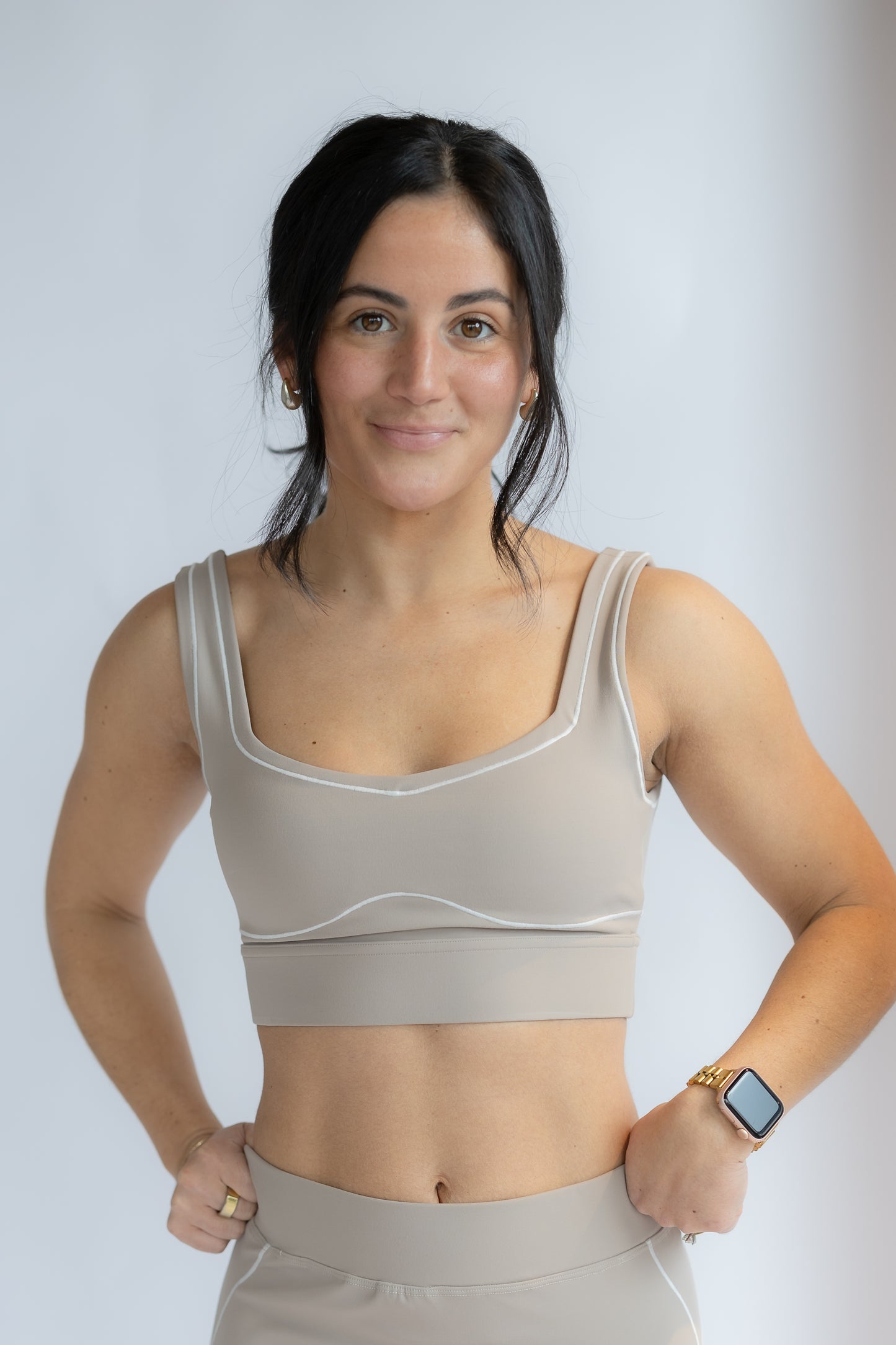 Woman wearing a beige sports bra and leggings on a plain background
