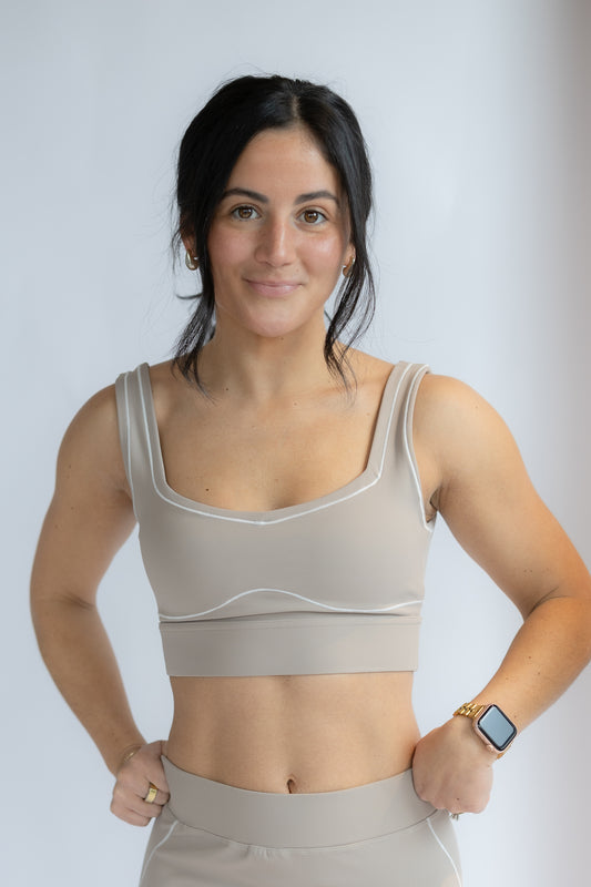 Woman wearing a beige sports bra and leggings on a plain background