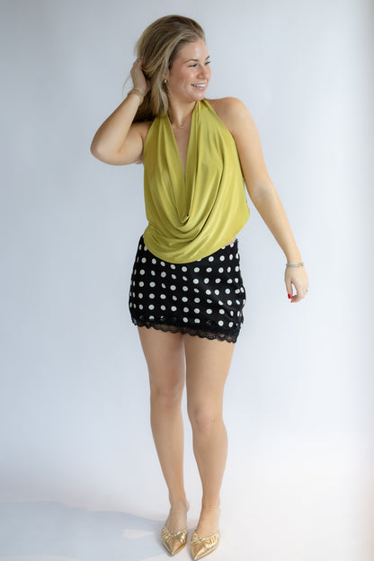 Woman wearing a yellow top and black polka dot skirt on a white background