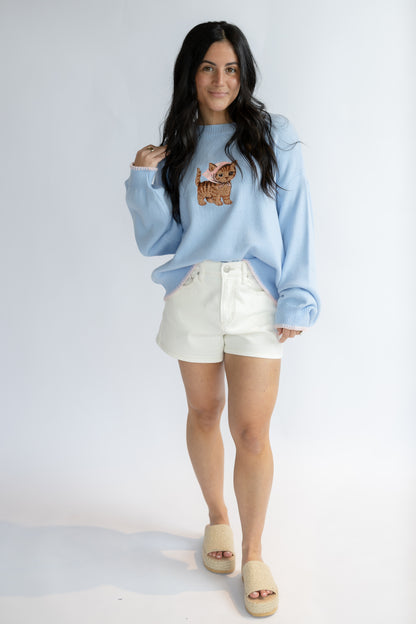 Woman wearing a light blue sweatshirt with a dog graphic and white shorts on a plain background