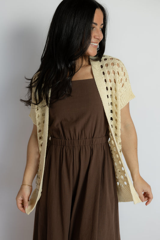 Woman wearing a brown dress with a beige crochet shrug against a plain background